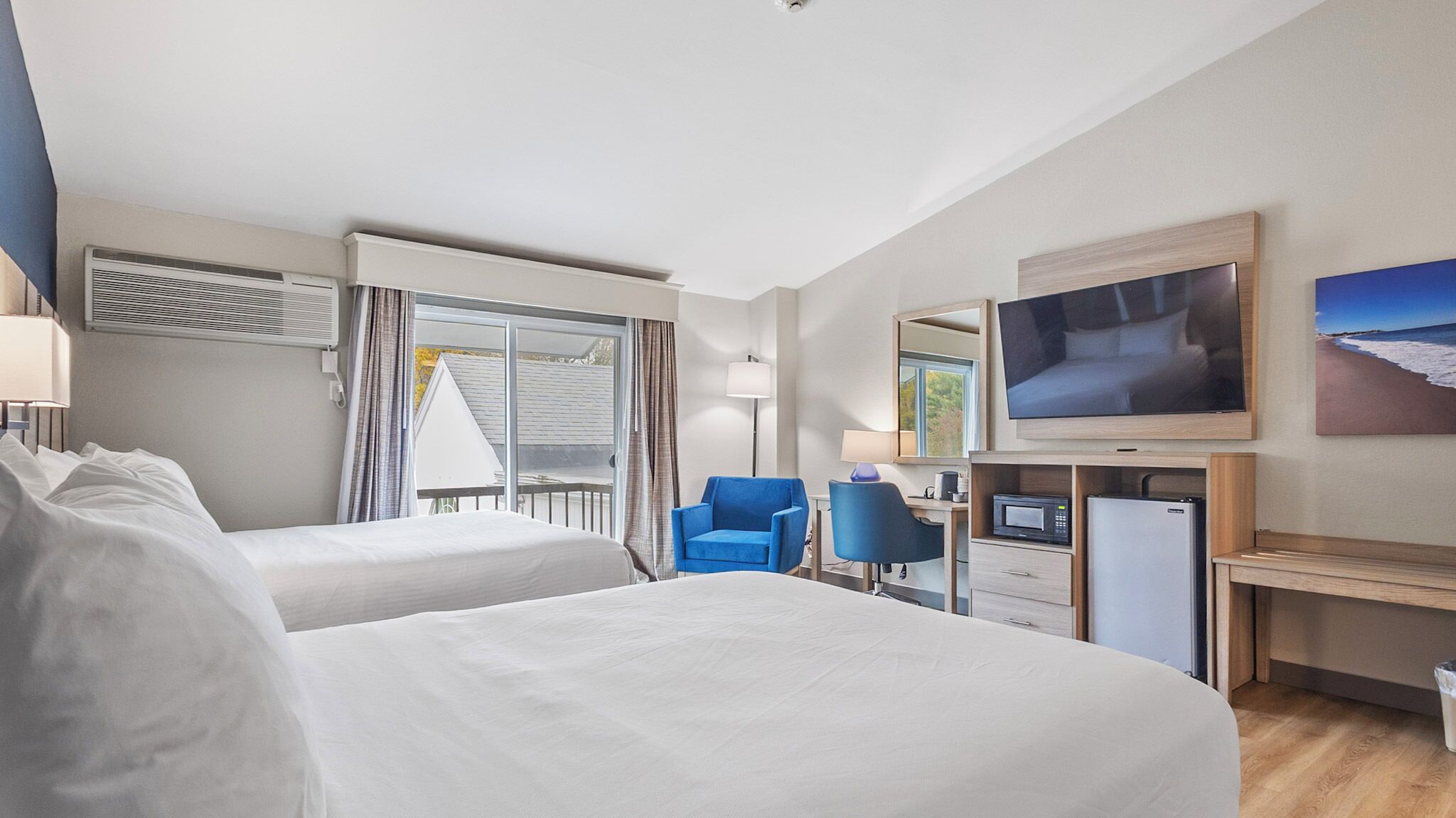 A hotel room with two beds, a desk with a computer, a TV, and a window with curtains.