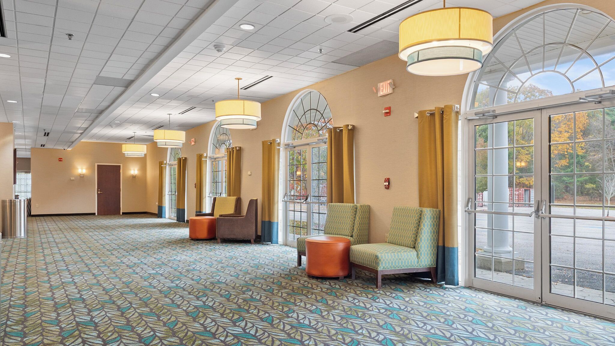 Un hall de hotel con alfombra estampada, zonas de estar, ventanas amplias e iluminación empotrada en el techo.