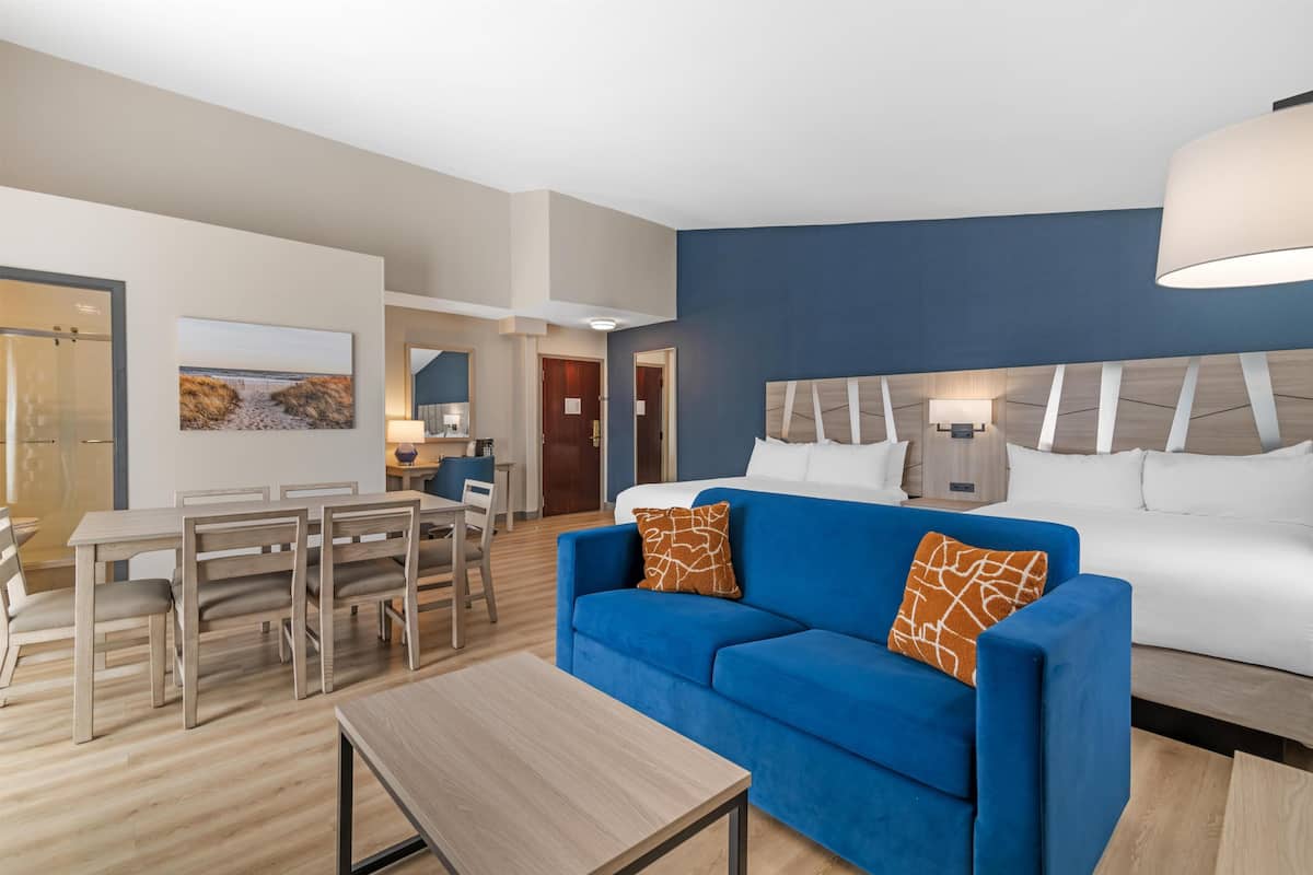 Ett modernt hotellrum med en blå soffa, ett matbord i trä och en stor säng.