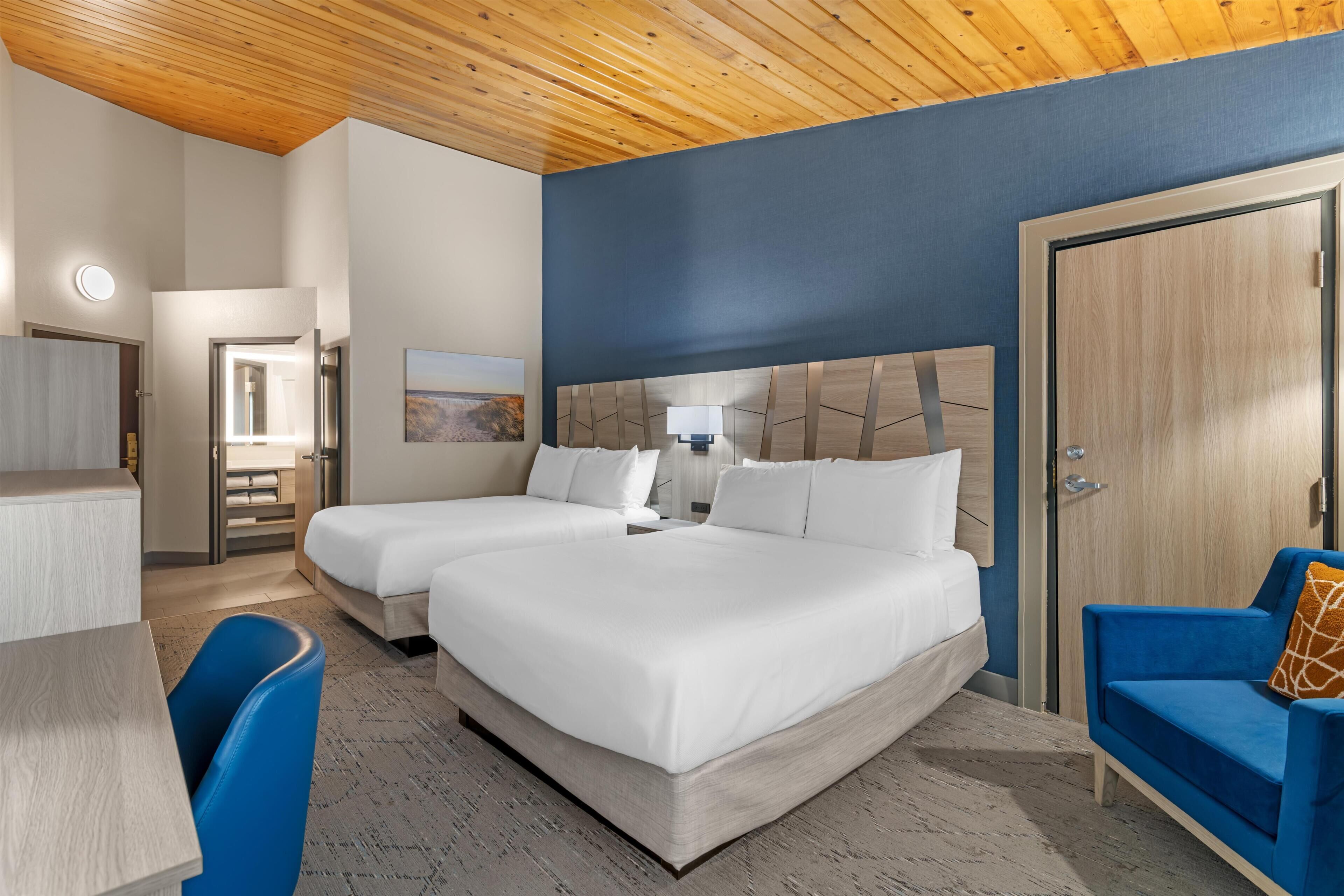 A hotel room with two beds, a desk, a chair, a wardrobe, and a door.