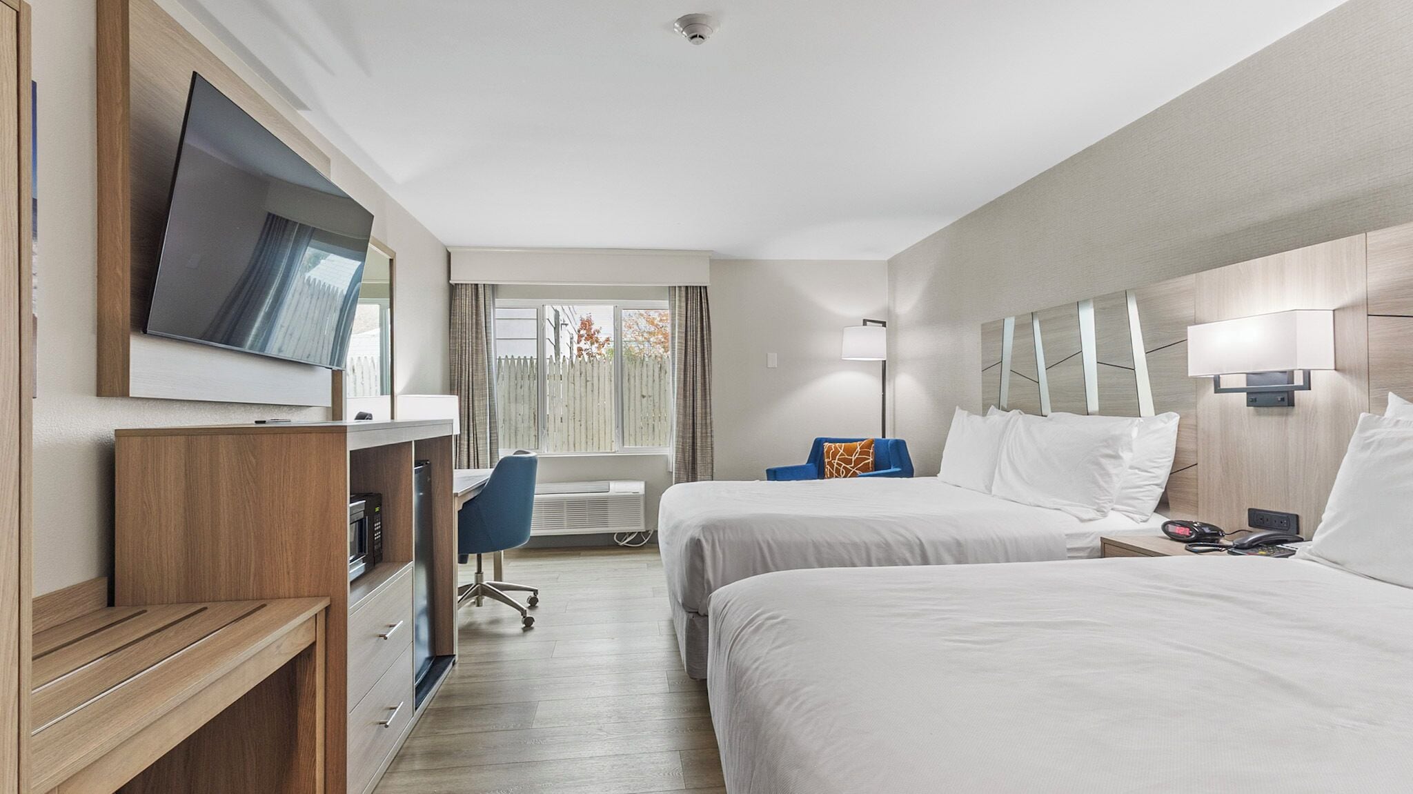 Ein Hotelzimmer mit zwei Betten, einem Schreibtisch, einem Fernseher und einem Fenster mit Vorhängen.