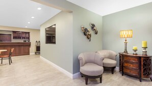Amplia sala de estar con una cocina al fondo, una mesa de comedor, dos sillones, una mesita de noche con una lámpara y decoración en la pared.