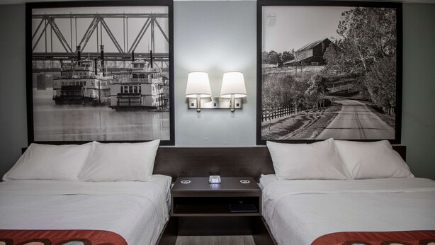Habitación de hotel con dos camas, una mesita de noche y dos lámparas fijadas a la pared.