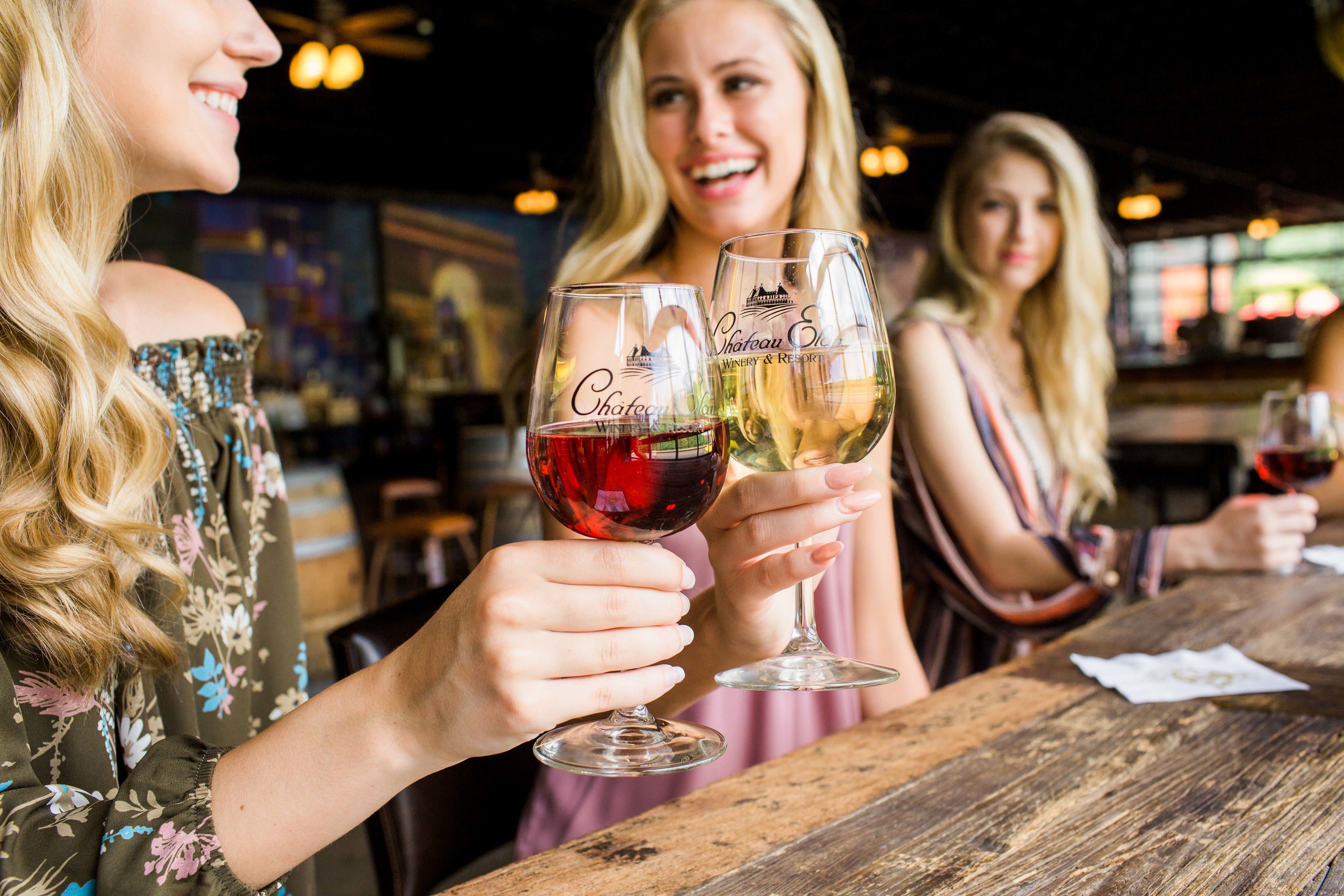 A bar setting with wooden tables and people holding glasses.