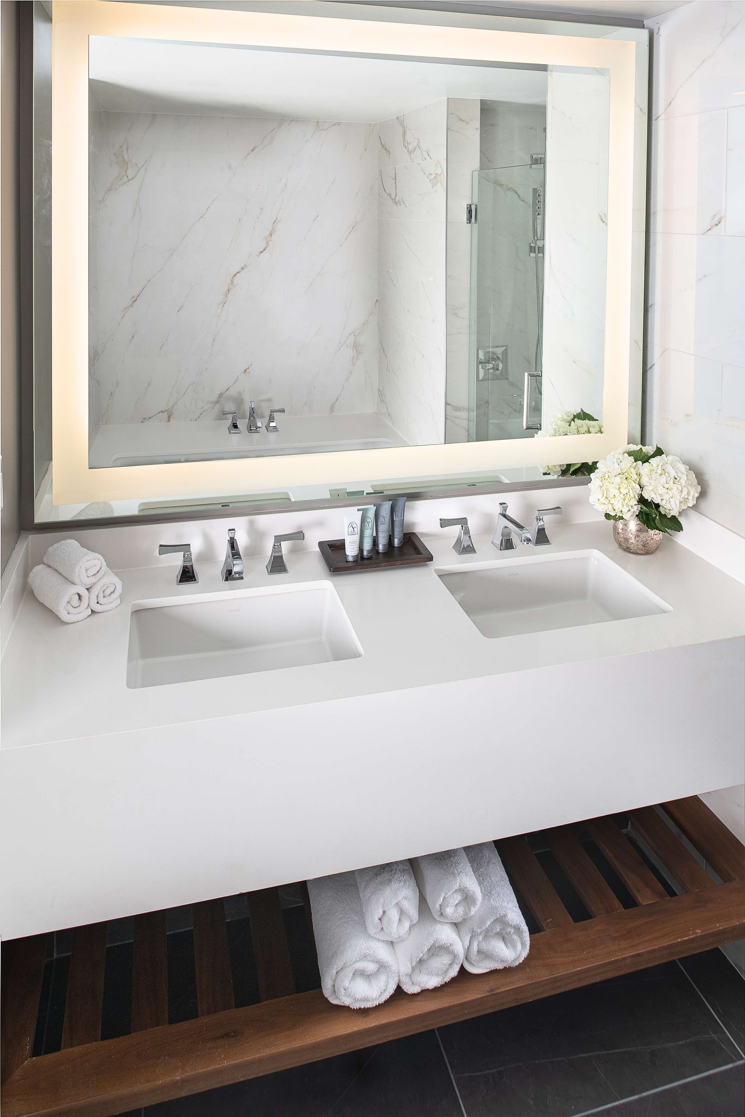 Un baño moderno con dos lavamanos, un espejo grande y un estante de madera con toallas.
