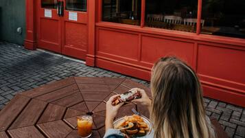 A person sitting at a wooden table outside a red building with a sign reading "PADDY'S BAR".