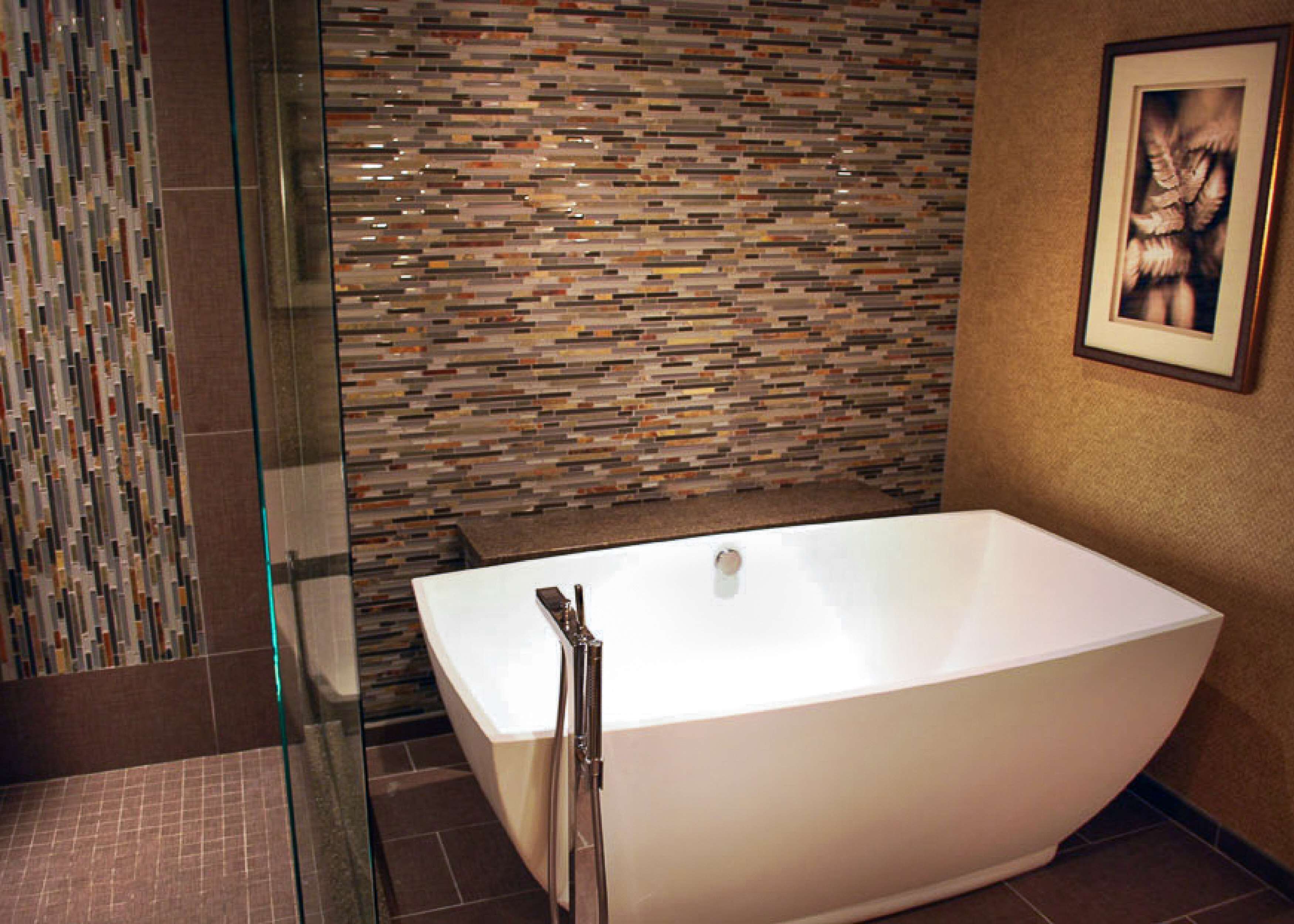 A modern bathroom with a freestanding bathtub, a glass shower enclosure, and a mosaic tile wall.