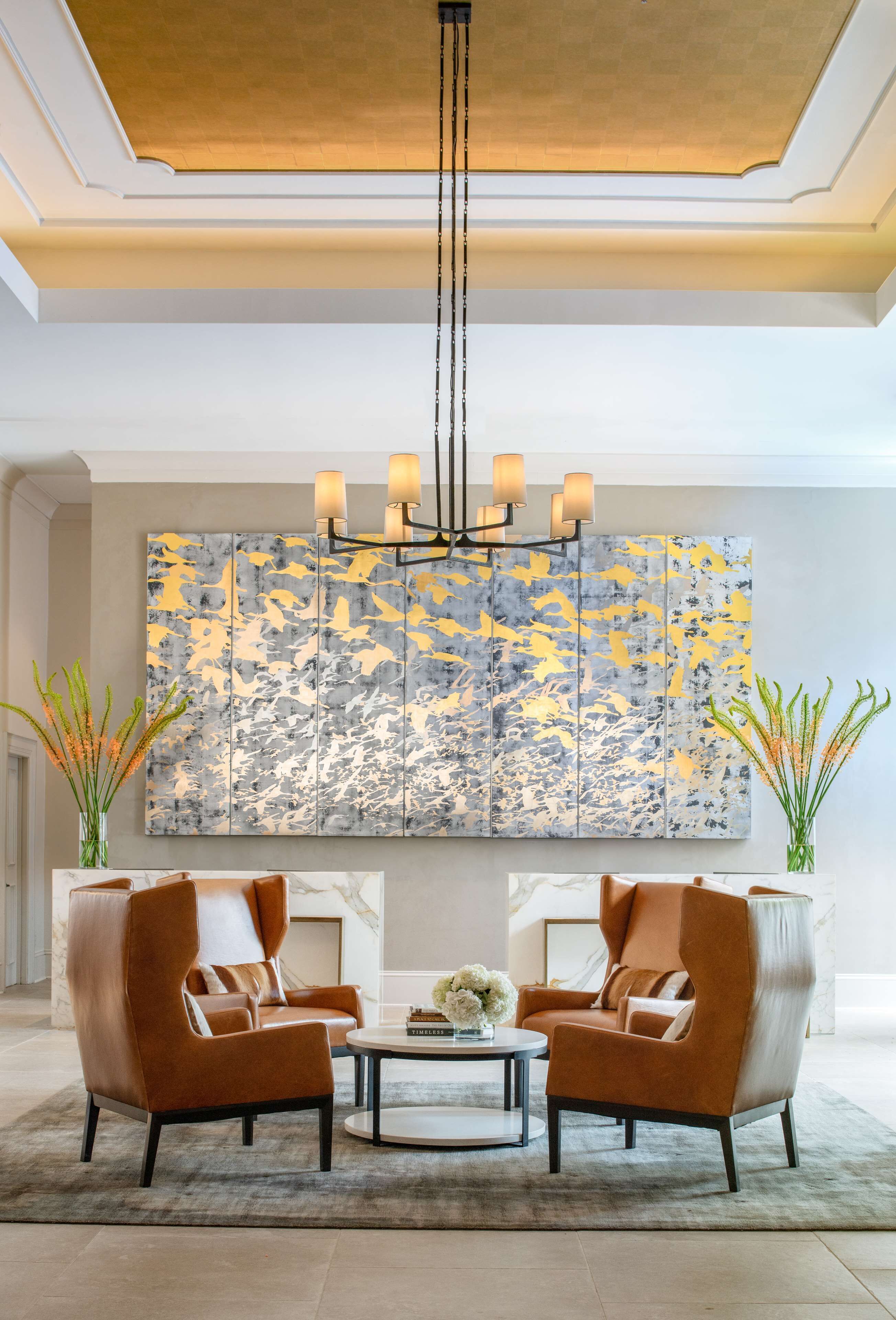 A modern living room with two brown armchairs, a round coffee table, and a large abstract painting on the wall.