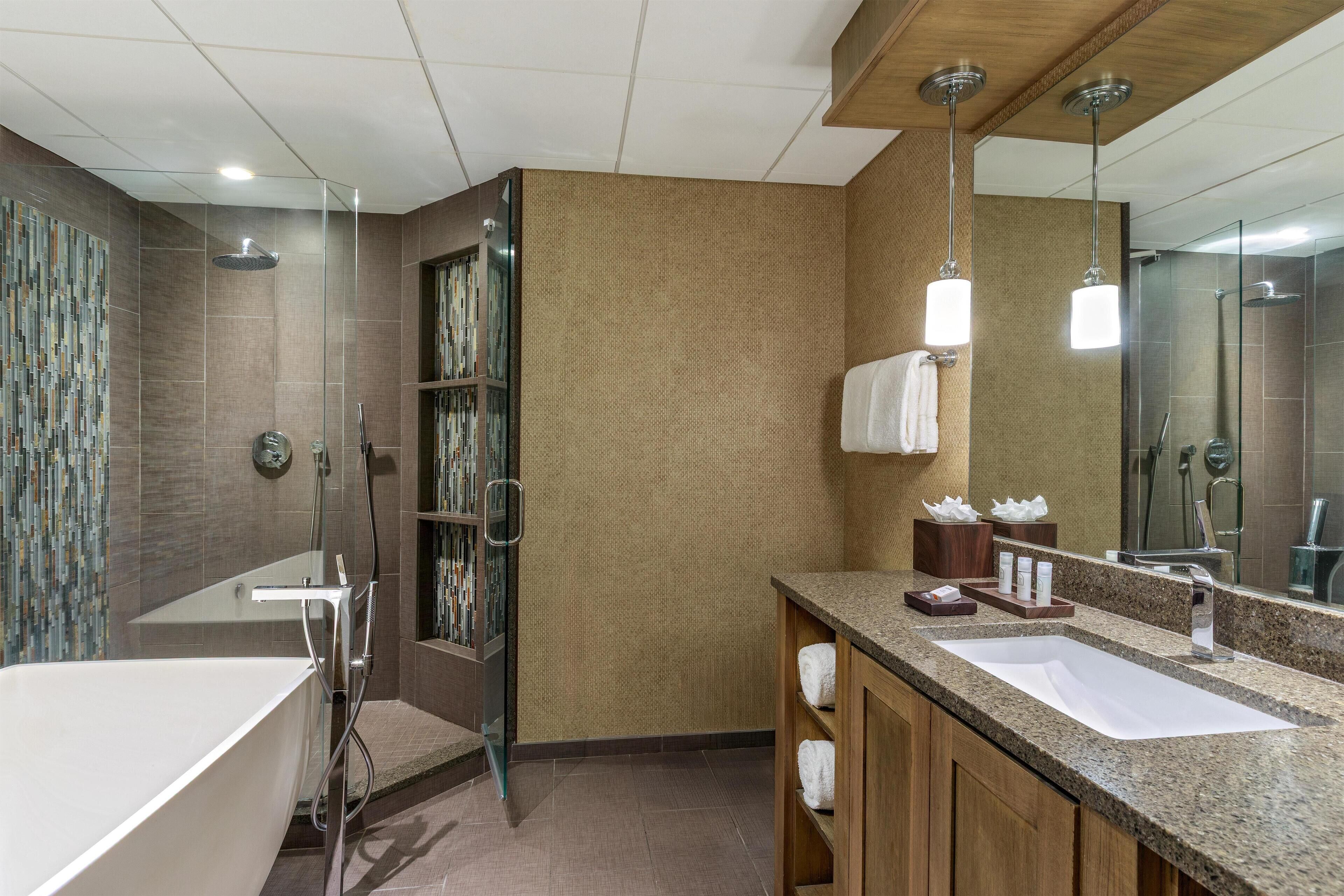 A modern bathroom with a bathtub, shower, and vanity with a large mirror.