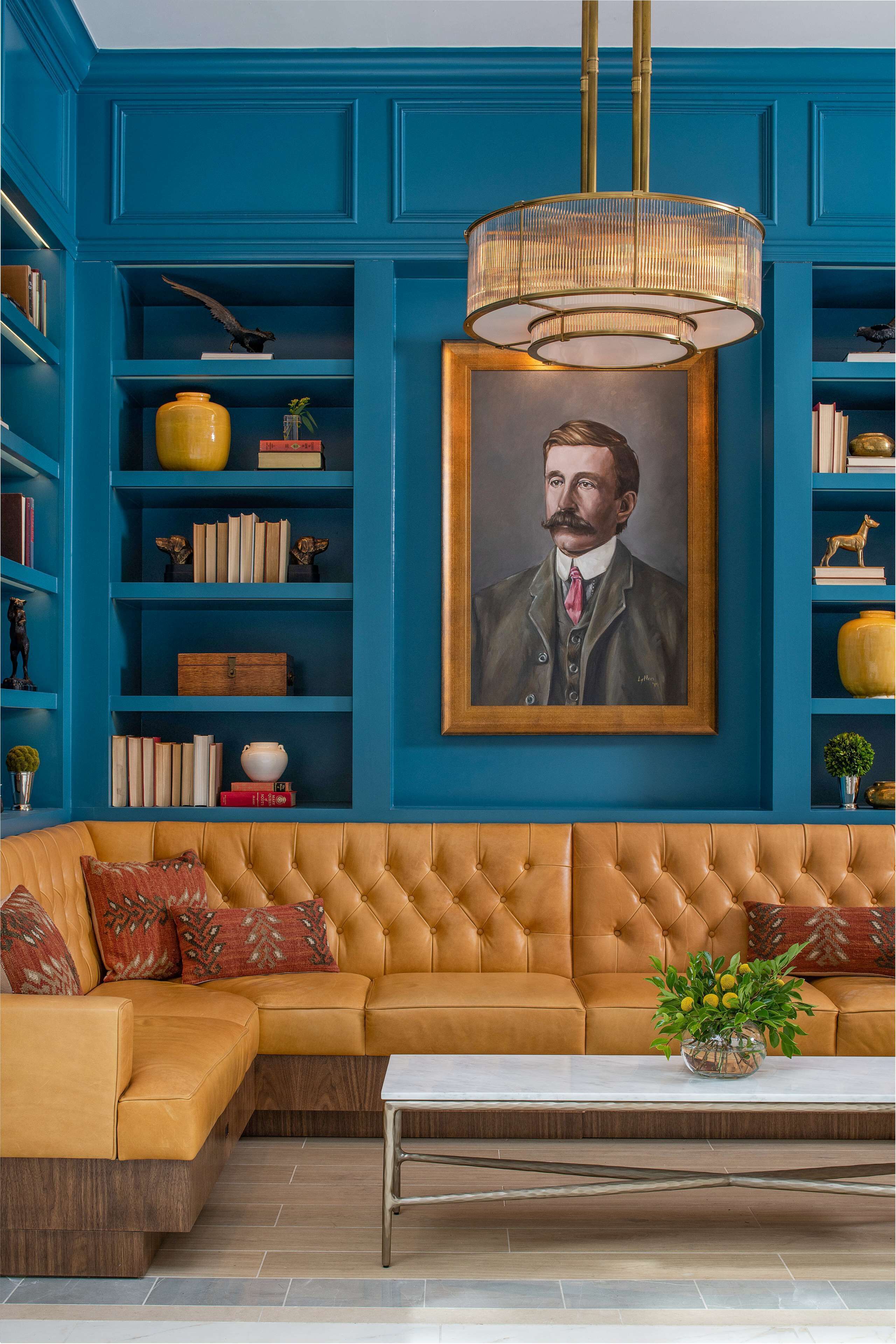 Une pièce avec un mur bleu, un grand portrait encadré, un canapé en cuir marron et une table basse blanche.