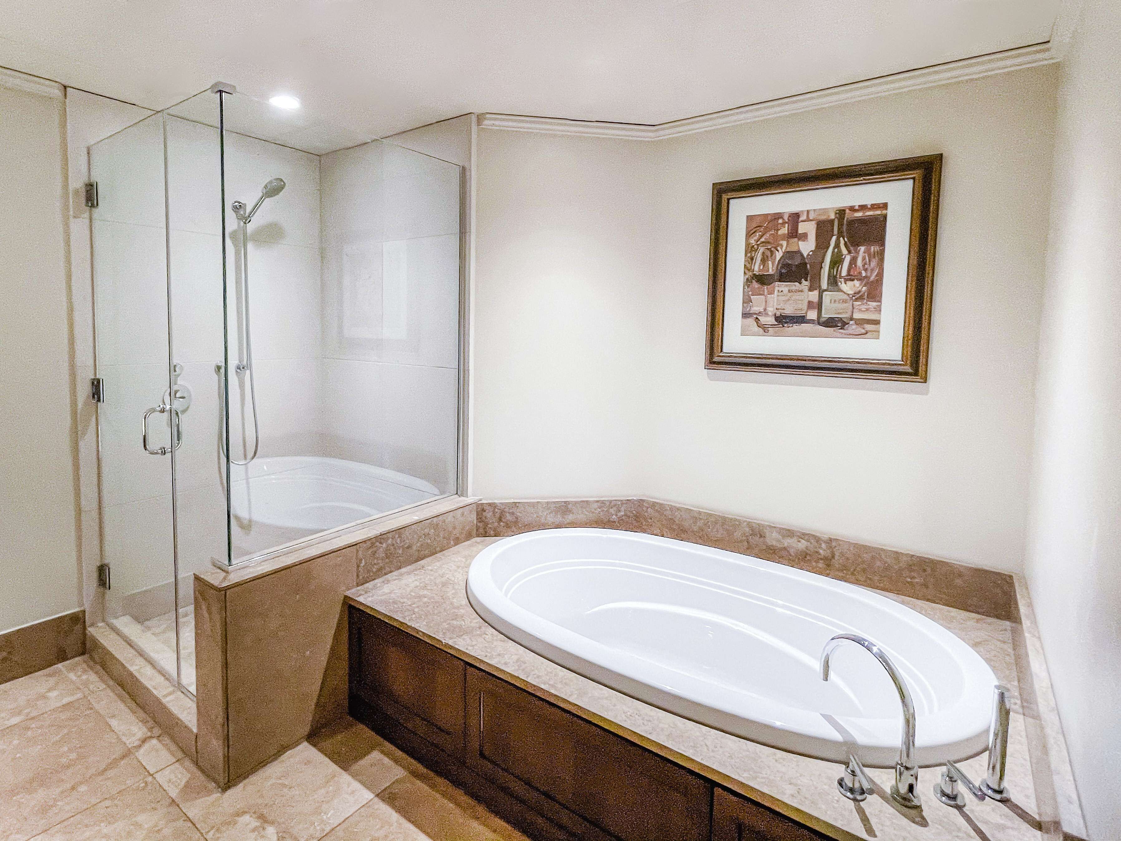 Un baño moderno con ducha envuelta en vidrio, una bañera independiente y un cuadro en la pared.