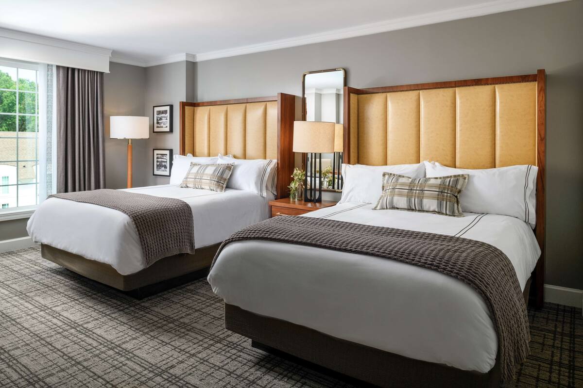 A hotel room with two beds, a large window, and a view of greenery outside.
