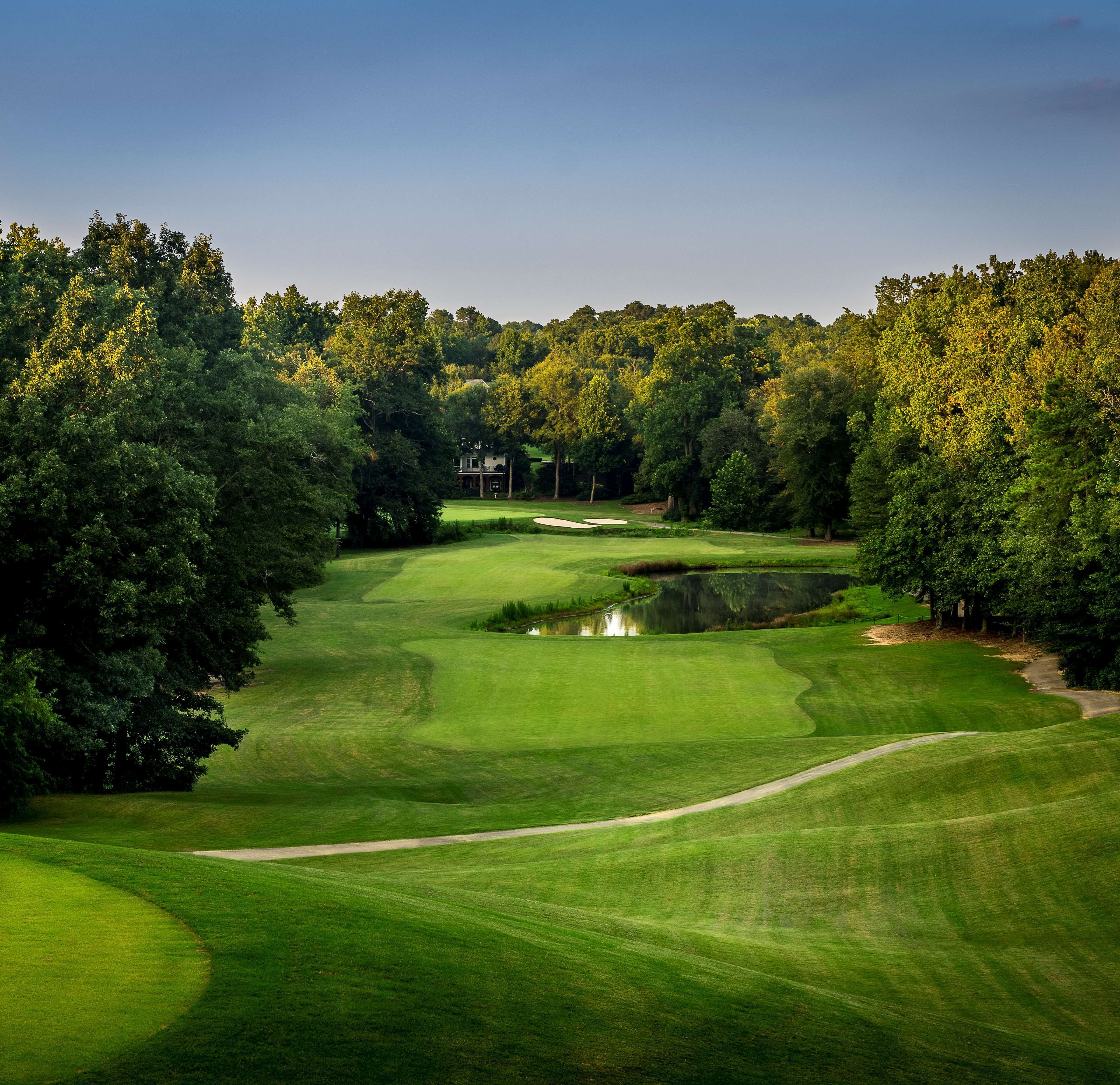 A golf course with a clubhouse, ponds, and dense trees.
