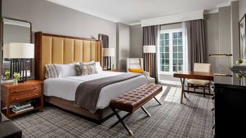 A hotel room with a large bed, a wooden nightstand, a bench, a desk, and a chair.