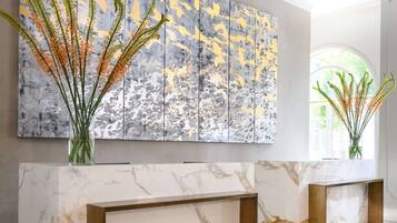 Um hall moderno com balcões de recepção em mármore, uma grande pintura abstrata e um vaso de vidro com plantas.