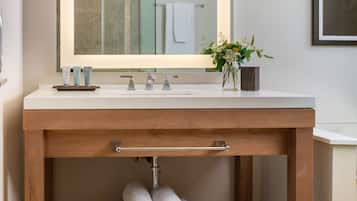 A bathroom with a wooden vanity, a large mirror, and a shelf with rolled towels.