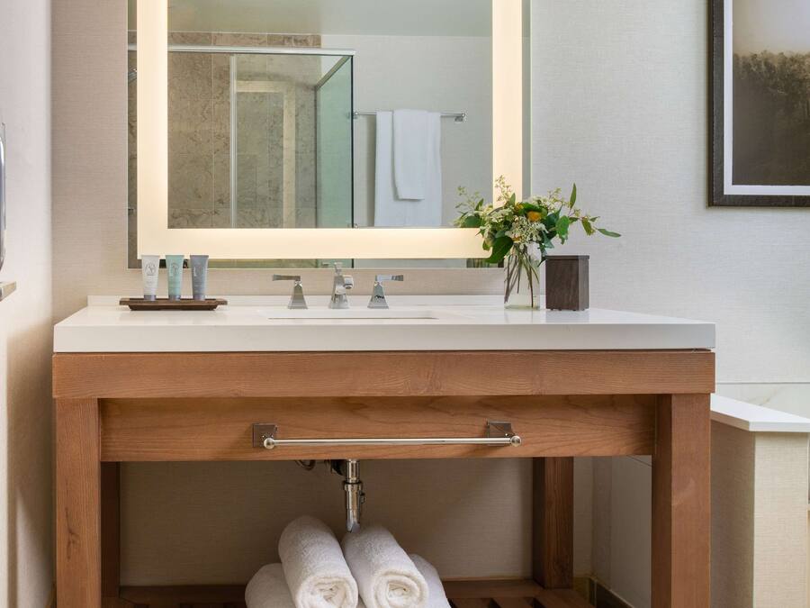 A bathroom with a wooden vanity, a large mirror, and a shelf with rolled towels.