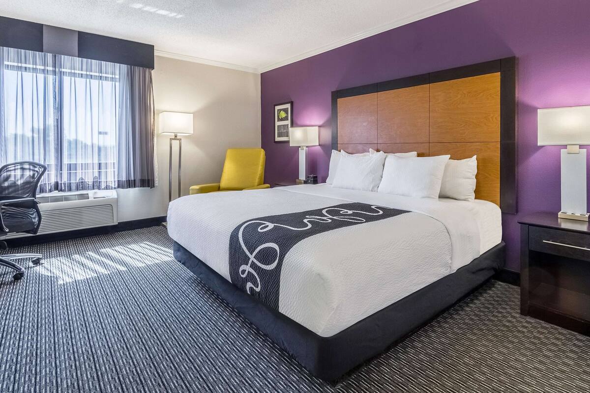 Une chambre d’hôtel avec un grand lit, une chaise, un bureau et une fenêtre avec des rideaux.