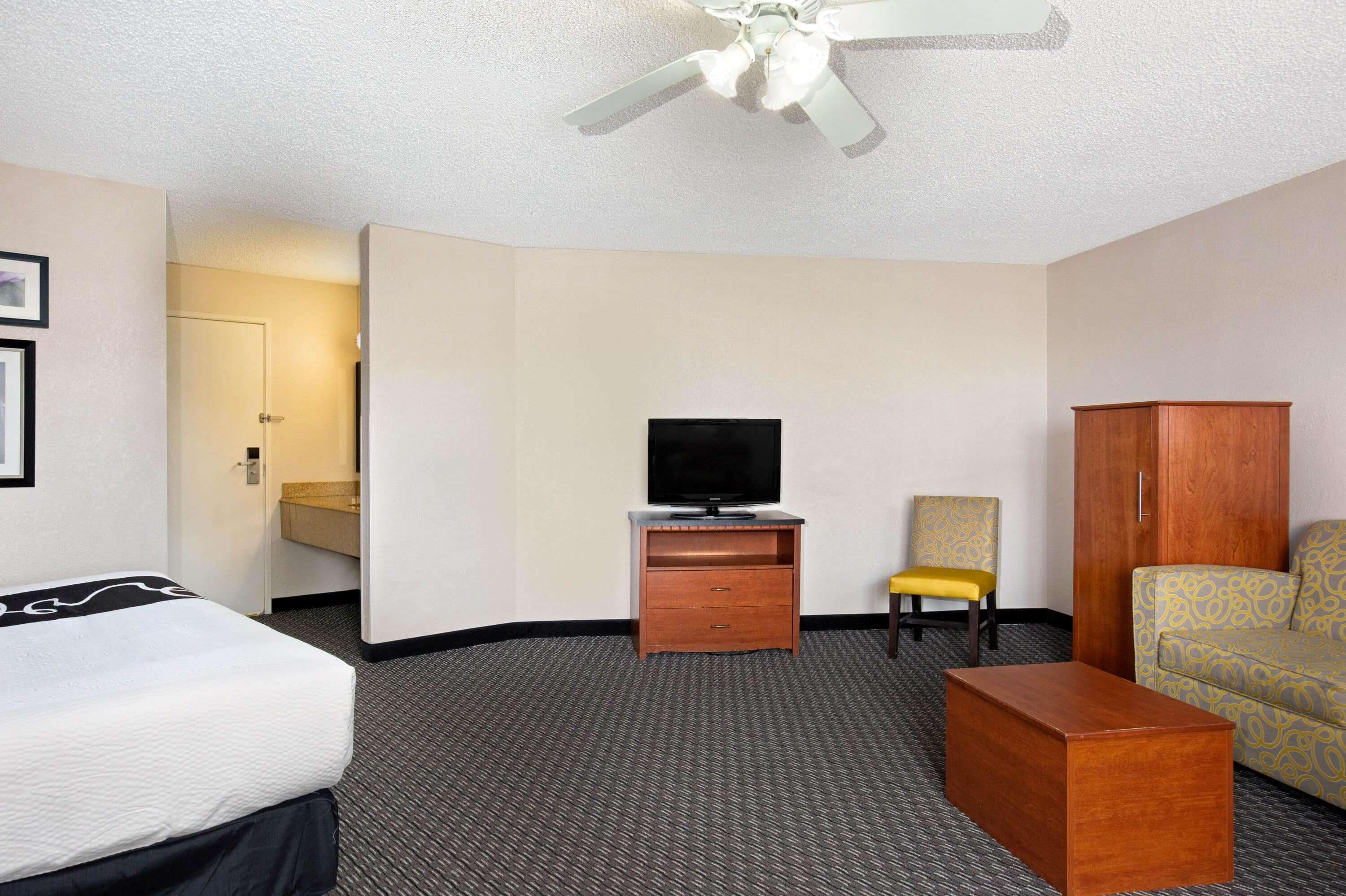 A hotel room with a bed, a TV on a wooden stand, a sofa, a chair, and a small table.