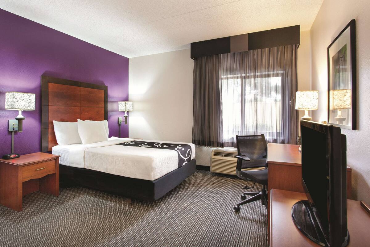 Une chambre d’hôtel comprenant un lit, un bureau, une chaise, une télévision et deux lampes.