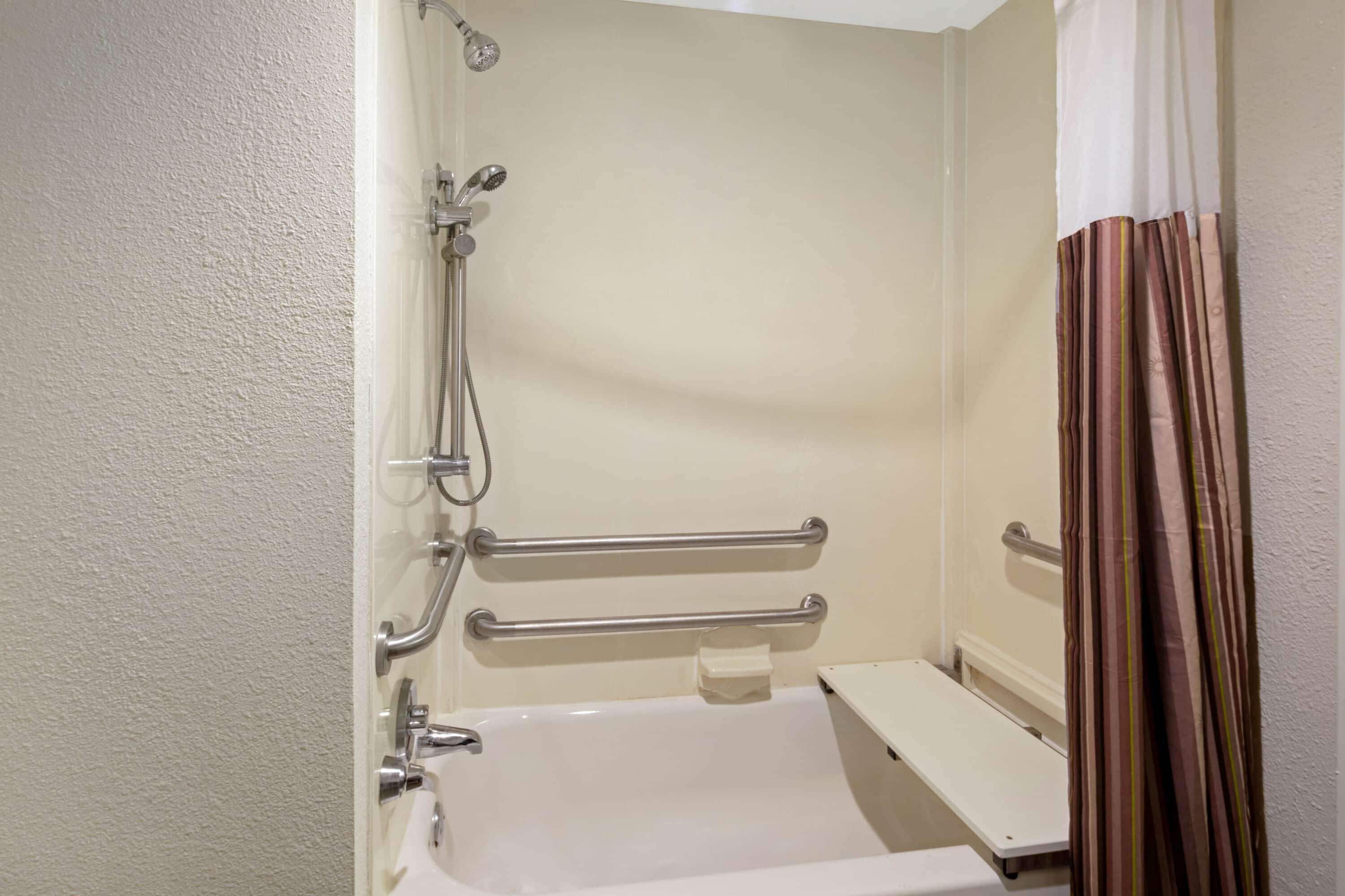 A bathroom with a bathtub, grab bars, and a showerhead.