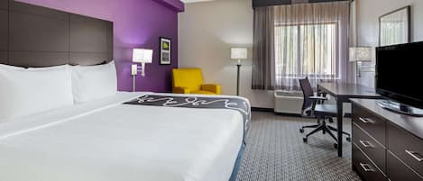 Une chambre d’hôtel avec un grand lit, un bureau, une chaise, une télévision et une fenêtre avec des rideaux.