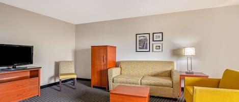 Una habitación de hotel con una televisión de pantalla plana, un sofá, un sillón amarillo, un armario de madera y una mesita de noche con una lámpara.