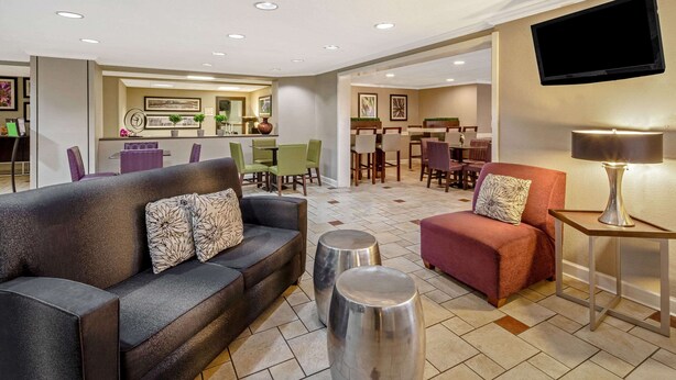 Un hall d’hôtel avec un canapé, un fauteuil et, au fond, un coin repas.