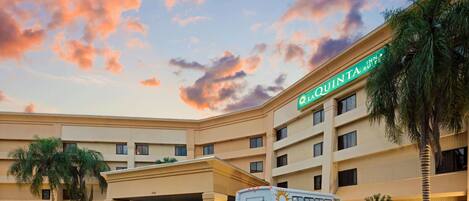 Un hotel con un letrero grande que dice "LA QUINTA INN & Suites" y un autobús blanco estacionado frente a él.