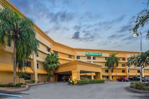 La Quinta Inn & Suites features a modern entrance with a covered area and lush surroundings.