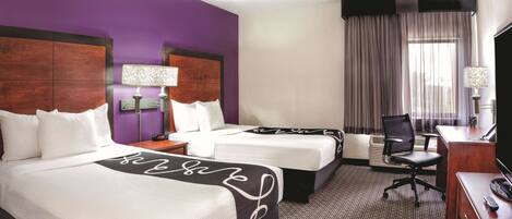 A hotel room with two beds, a desk, a chair, and a television.