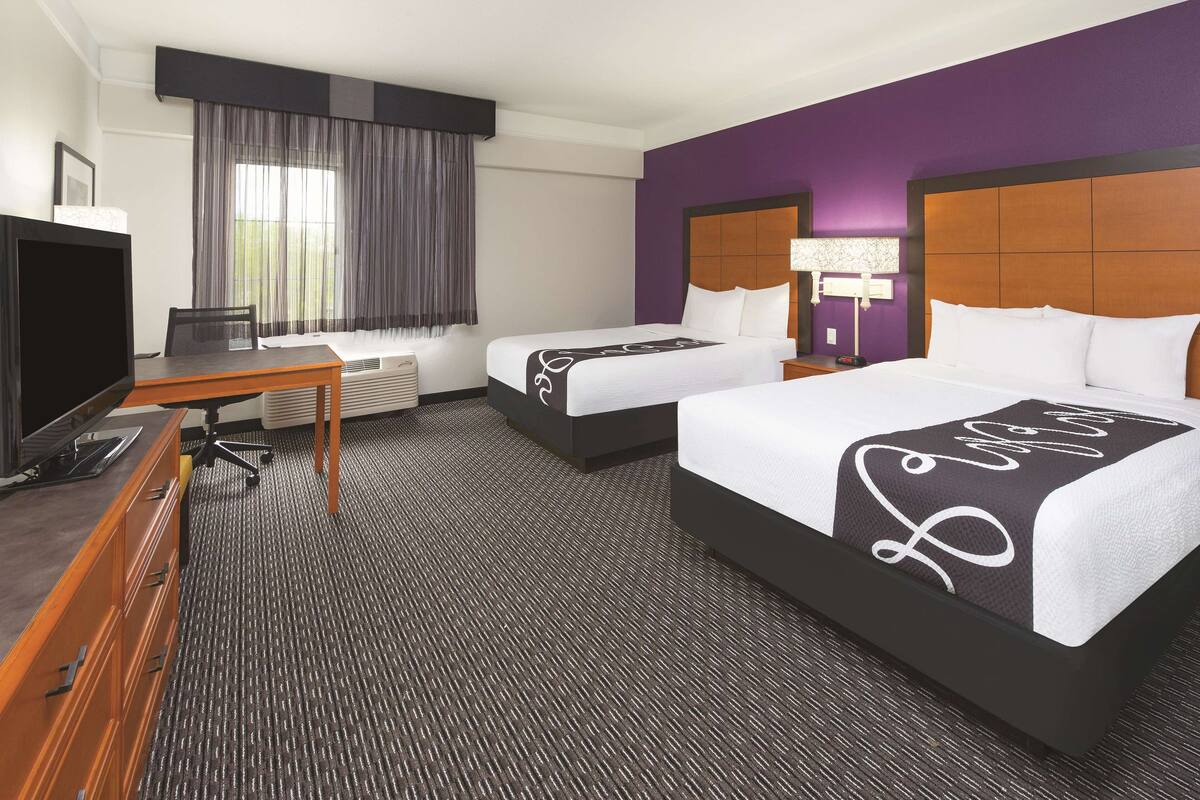 Une chambre d’hôtel avec deux lits, un bureau avec un ordinateur, une télévision et une fenêtre avec des rideaux.