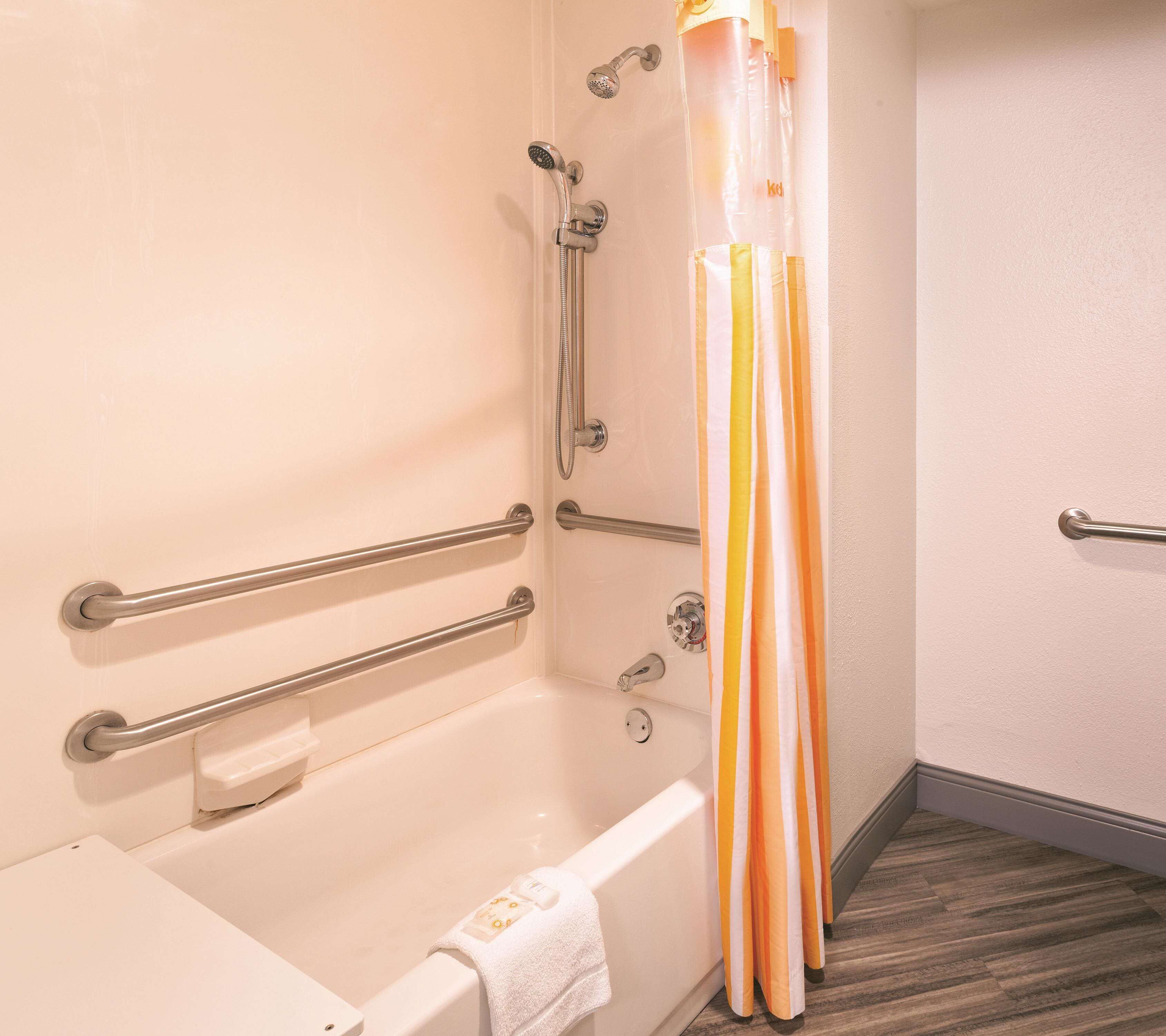 Un bagno con una vasca, maniglie di sostegno, una doccetta e un telo da doccia a righe.