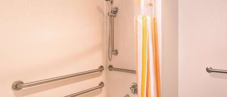 A bathroom with a bathtub, grab bars, a showerhead, and a striped shower curtain.