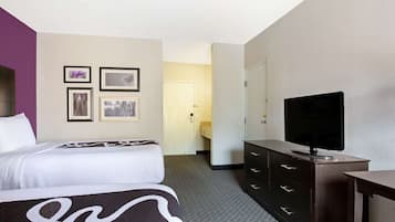 A hotel room with a bed, a dresser, a television, and framed pictures on the wall.