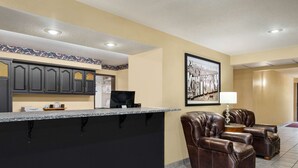 A hotel lobby with a reception desk, leather armchairs, a framed picture on the wall, and a tiled floor.