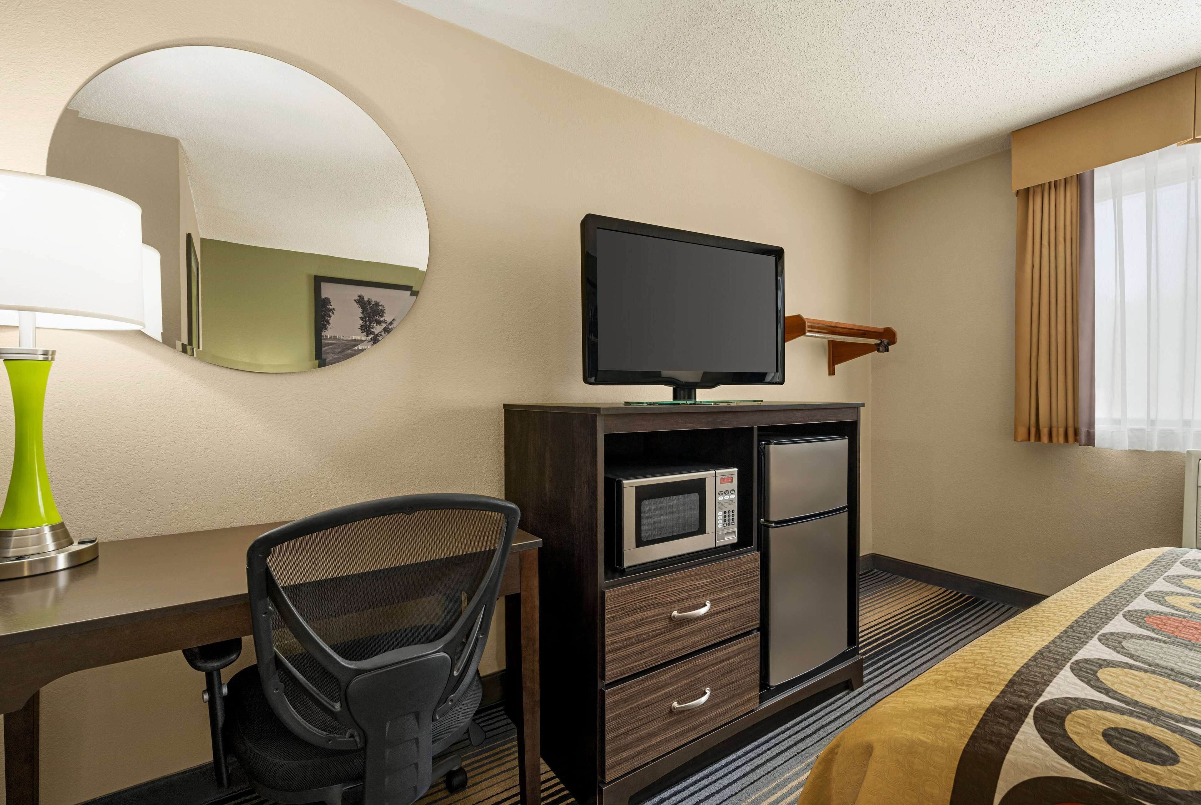 A hotel room with a desk, chair, television, microwave, and a bed.