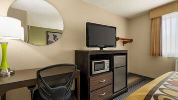 A hotel room with a desk, chair, television, microwave, and a bed.