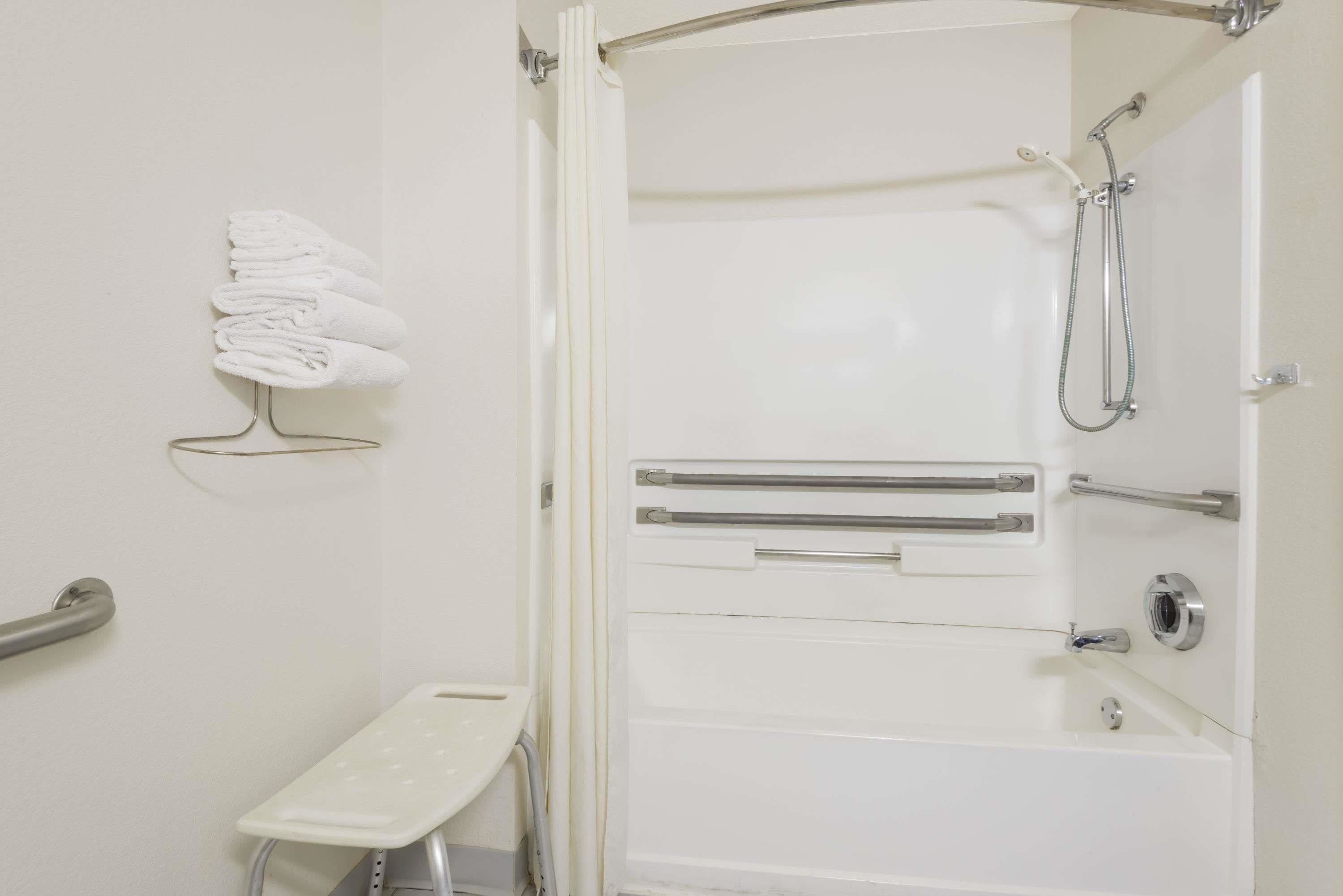 A bathroom with a shower, grab bars, a towel rack, and a small bench.