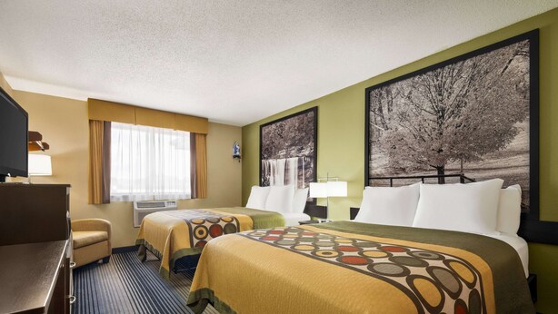 A hotel room with two beds, a desk, a chair, and a large window with curtains.