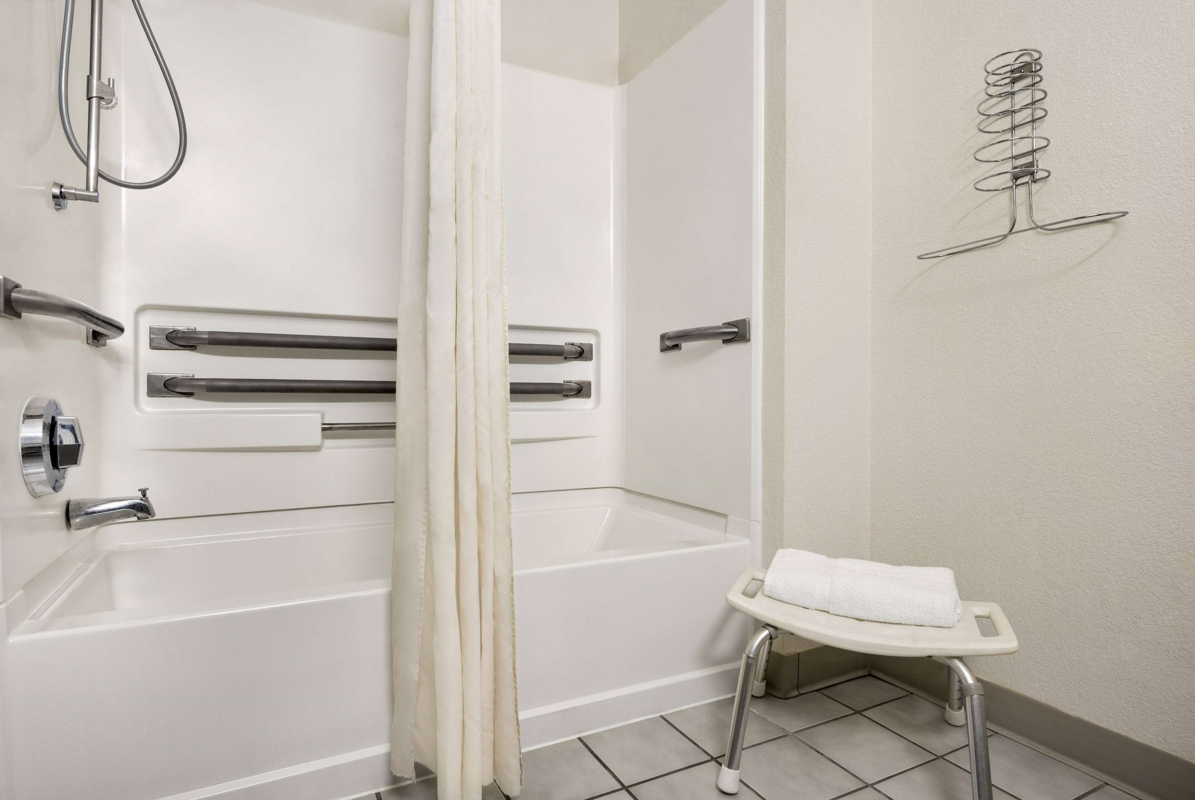 A bathroom with a bathtub, a shower, and a small stool with a towel.