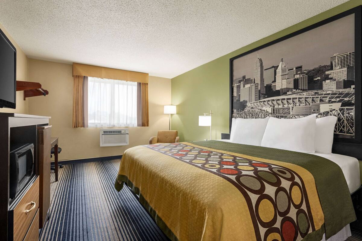 Una habitación de hotel con una cama, televisor, escritorio y ventana con cortinas.