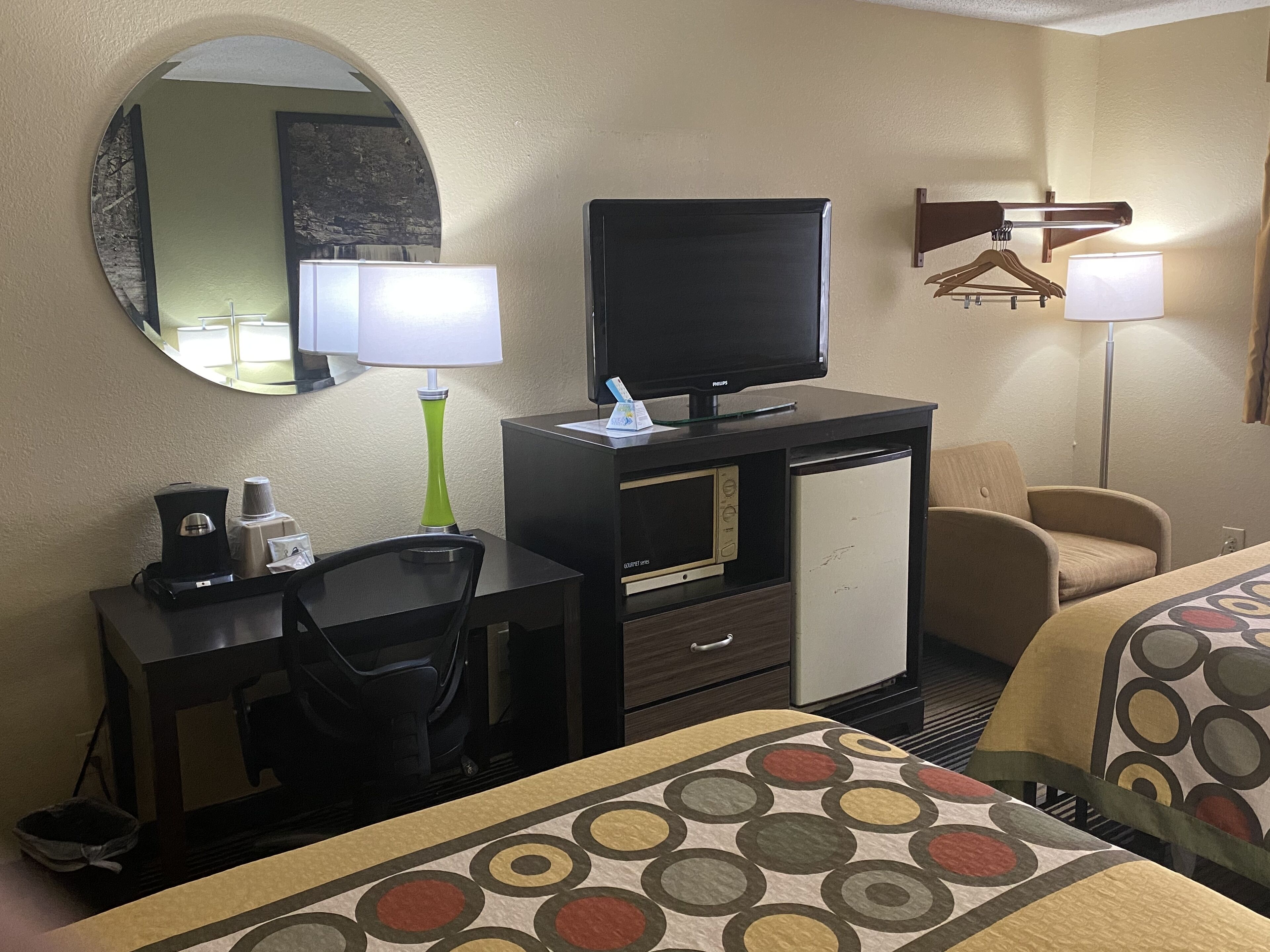 A hotel room with a television, desk, chair, and two beds with patterned bedspreads.