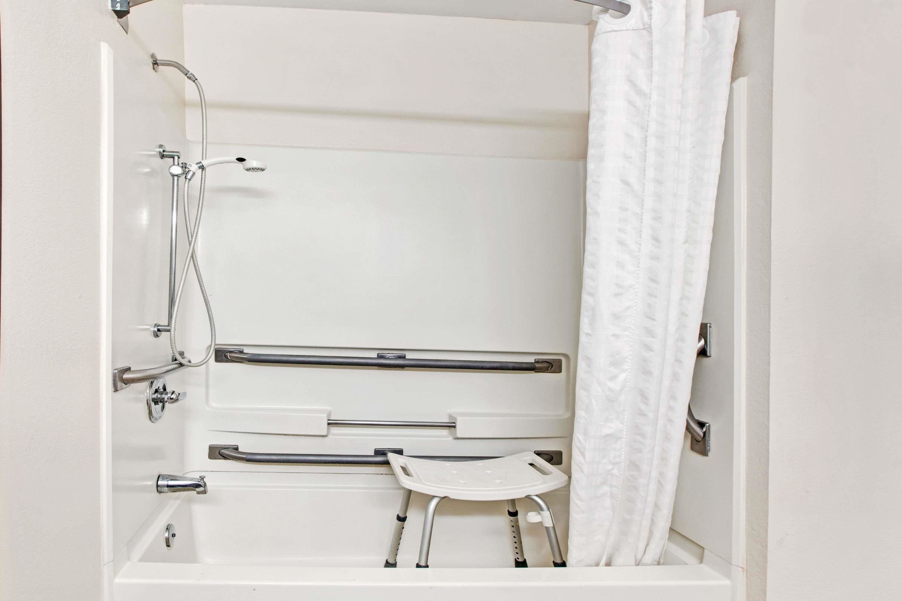 A bathroom with a bathtub, shower, grab bars, and a white towel rack.