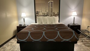 Habitación de hotel con una cama grande, dos mesitas de noche con lámparas, cabecera con una imagen de un paisaje urbano y suelo de parquet de madera.