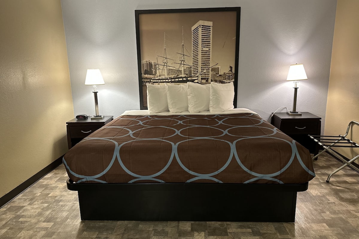 A hotel room with a large bed, two bedside tables with lamps, a headboard with a cityscape picture, and a wooden parquet floor.