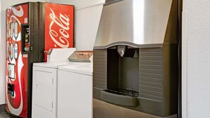 Cocina compacta con lavadora, máquina expendedora de Coca-Cola y refrigerador de acero inoxidable.