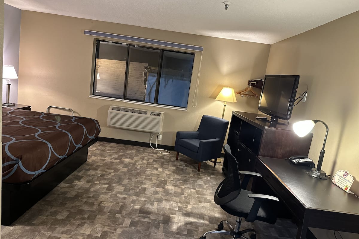 A hotel room with a bed, desk, chair, TV, and a window with blinds.