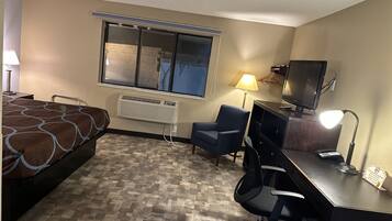 A hotel room with a bed, desk, chair, TV, and a window with blinds.
