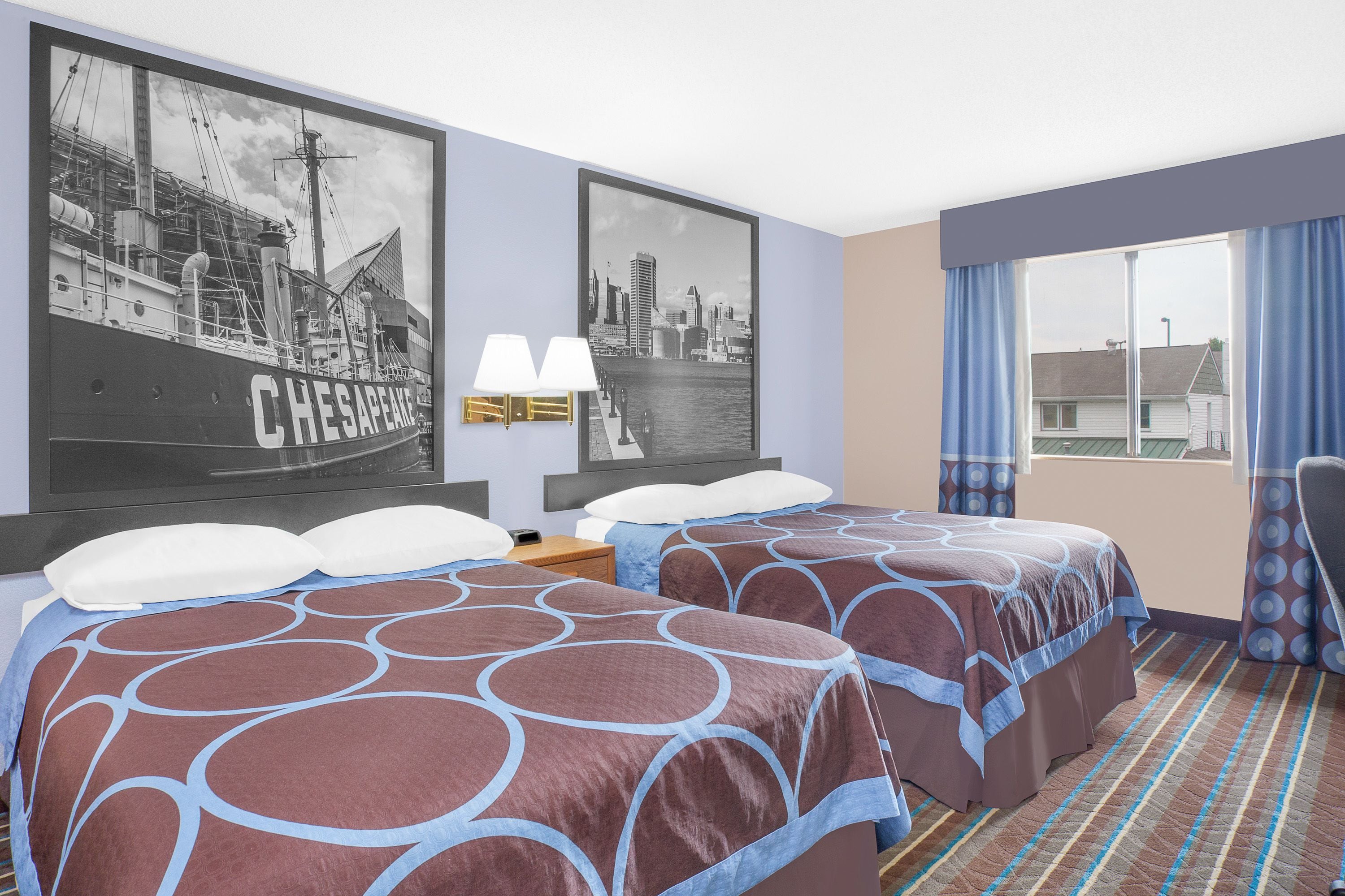 A hotel room with two beds, a cityscape poster, a window with curtains, and a striped carpet.